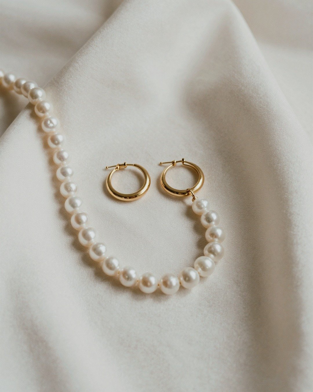 Pearls and gold hoop earrings arranged on ivory fabric