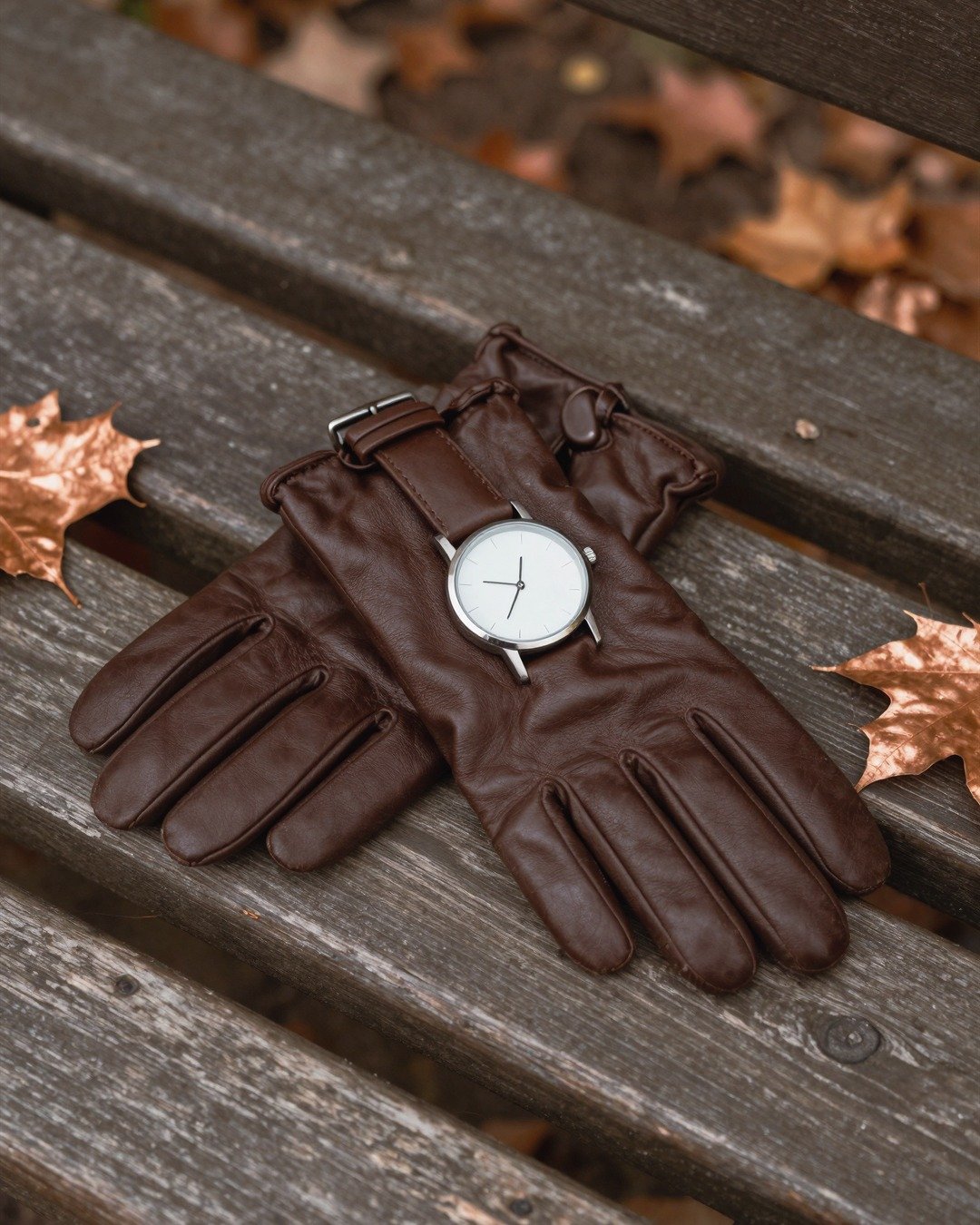 Leather gloves, a watch and autumn leaves on a wooden bench
