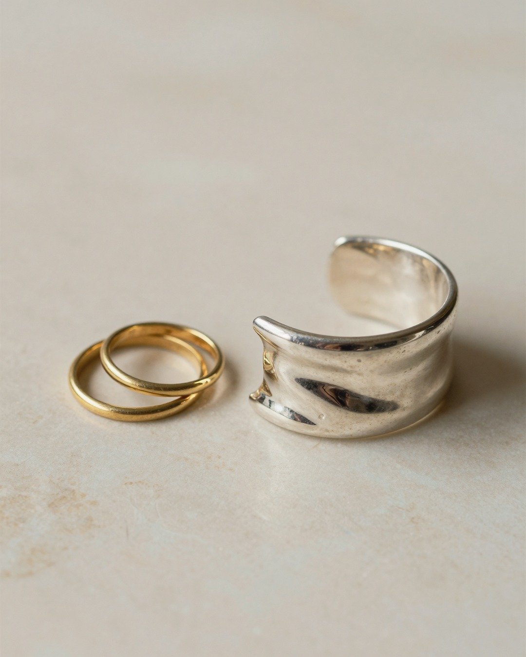 Gold rings and a silver cuff on pale stone